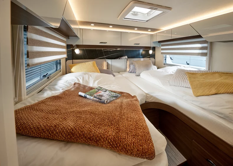 Innenansicht eines Wohnmobils mit zwei Einzelbetten, dekoriert mit Kissen und Decken.