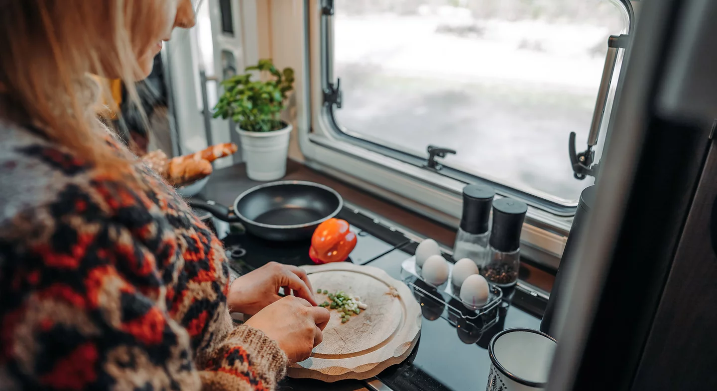 Person schneidet Gemüse in einer Camper-Küche.