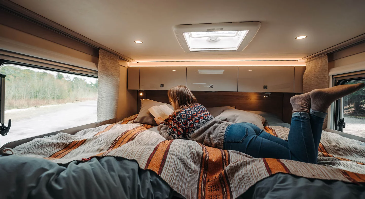 Eine Person liegt in einem gemütlichen Bett in einem Wohnmobil und liest ein Buch.