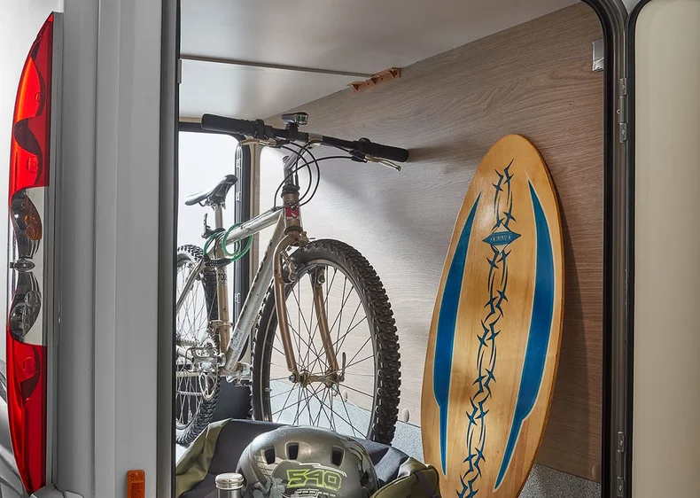 Ein Fahrrad und ein Surfbrett sind in einem Camper-Stauraum verstaut.