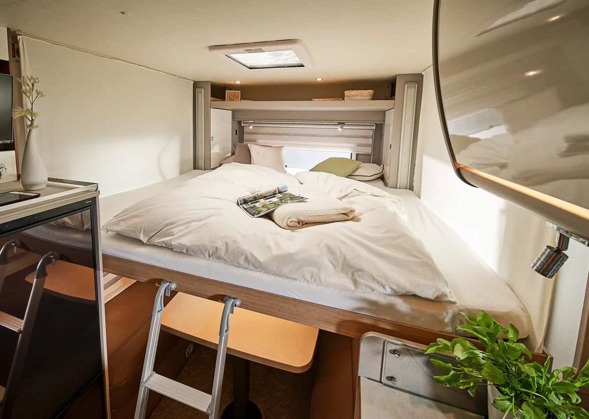 Innenraum eines Wohnmobils mit einem gemütlichen Doppelbett und einer kleinen Leiter.