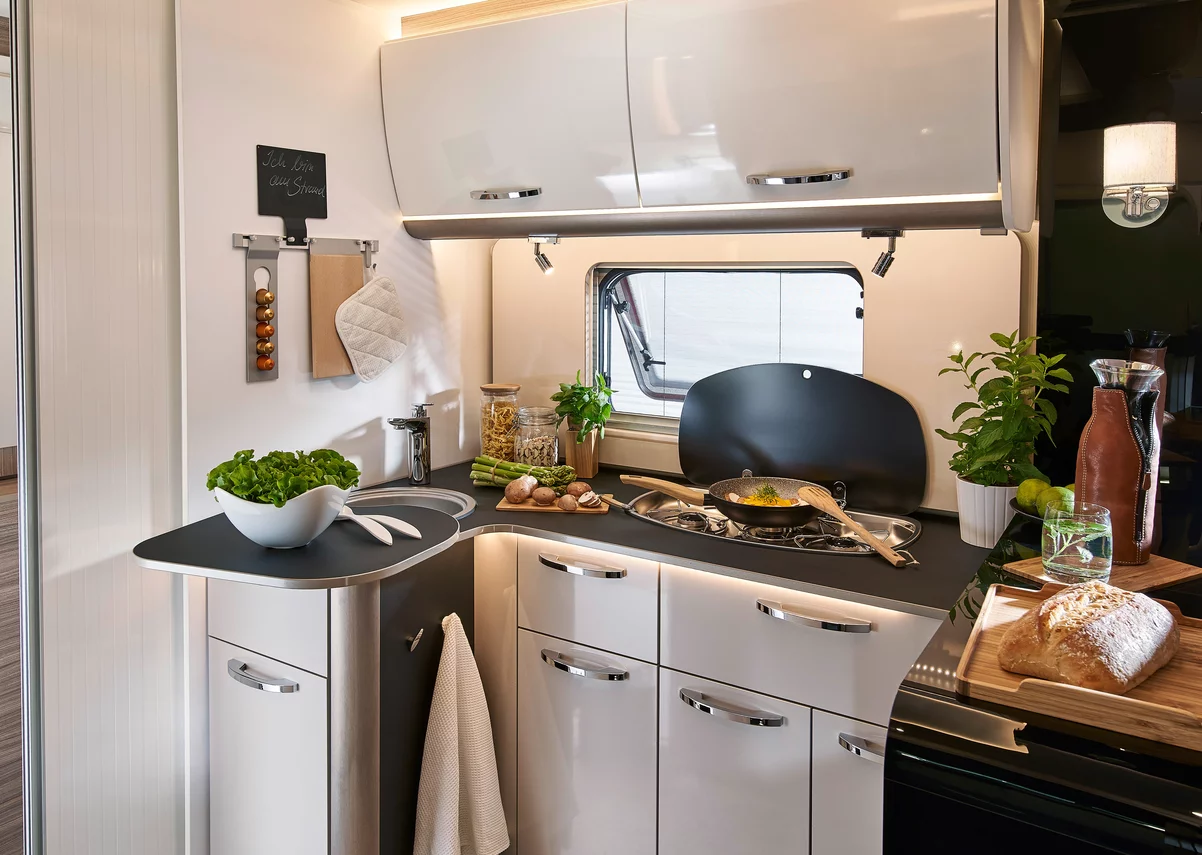 Moderne Wohnmobilküche mit Herd, Spüle und frischen Zutaten.