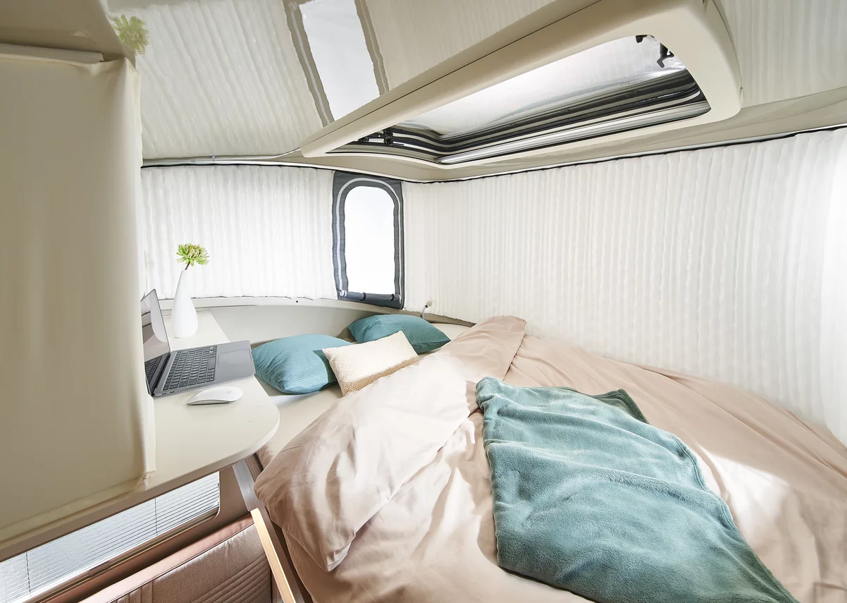 Innenraum eines Wohnmobils mit einem Bett, Laptop und Kissen.