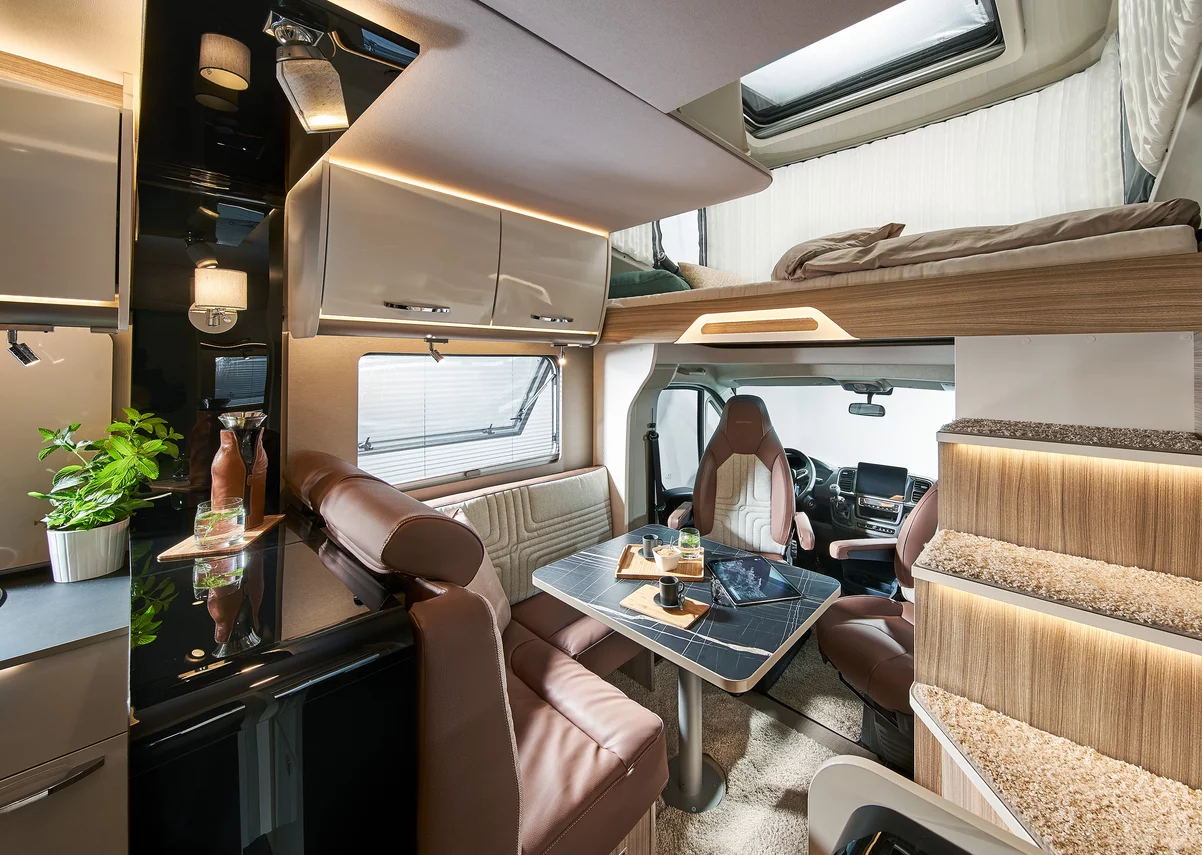 Innenansicht eines modernen Wohnmobils mit Sitzecke, Tisch, Küchenbereich und Hochbett.