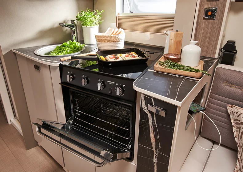 Kompakte Küche in einem Wohnmobil mit offenem Ofen und frischen Zutaten auf der Arbeitsfläche.
