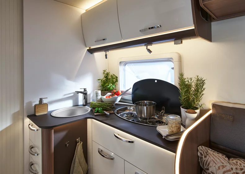 Innenansicht einer modernen Wohnmobilküche mit Herd, Spüle und frischen Zutaten.