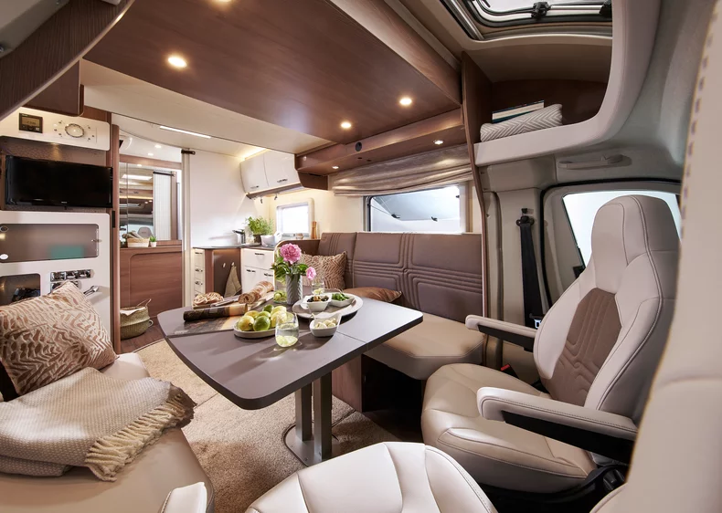Innenraum eines modernen Wohnmobils mit Tisch, Sitzecke und Küche.
