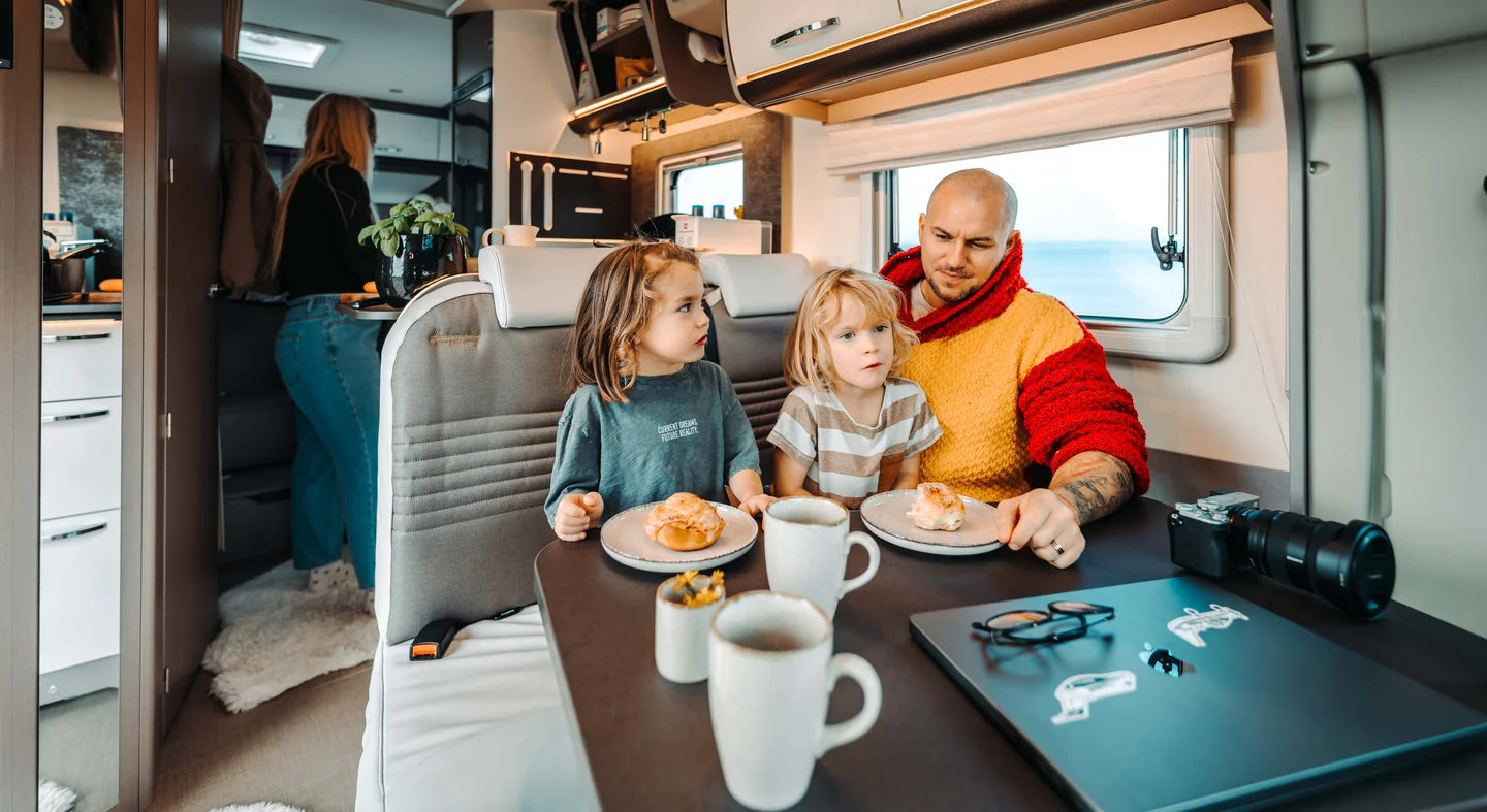 Eine Familie sitzt in einem Wohnmobil am Tisch und isst Gebäck.