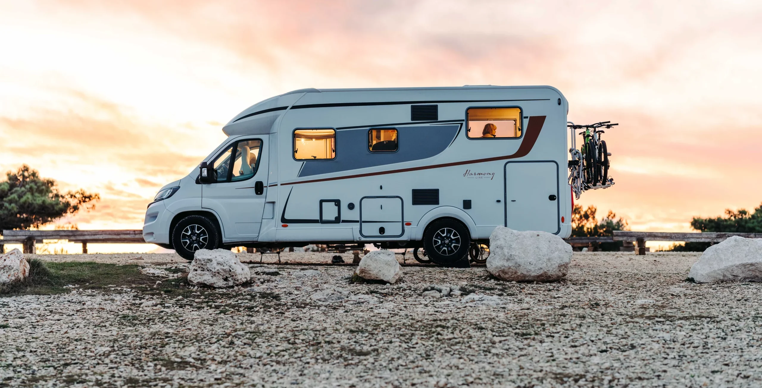 Ein weißes Wohnmobil der Marke Lyseo Harmony Line steht bei Sonnenuntergang auf einem steinigen Gelände.