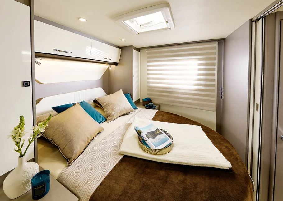 Gemütliches Schlafzimmer in einem Wohnmobil mit einem großen Bett und dekorativen Kissen.