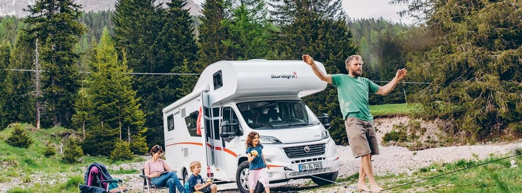 Eine Familie entspannt vor einem Sunlight A70 Wohnmobil in einer Waldlandschaft.