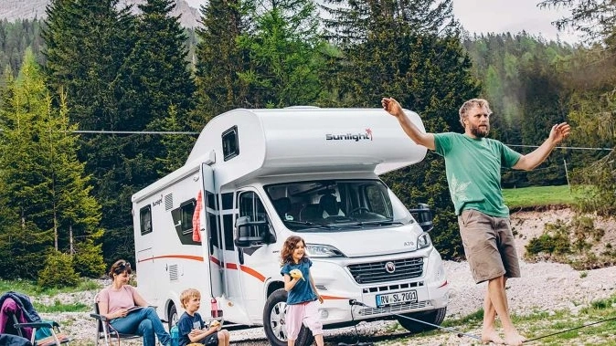 Eine Familie entspannt sich neben einem Sunlight A70 Wohnmobil in einer Waldlandschaft.