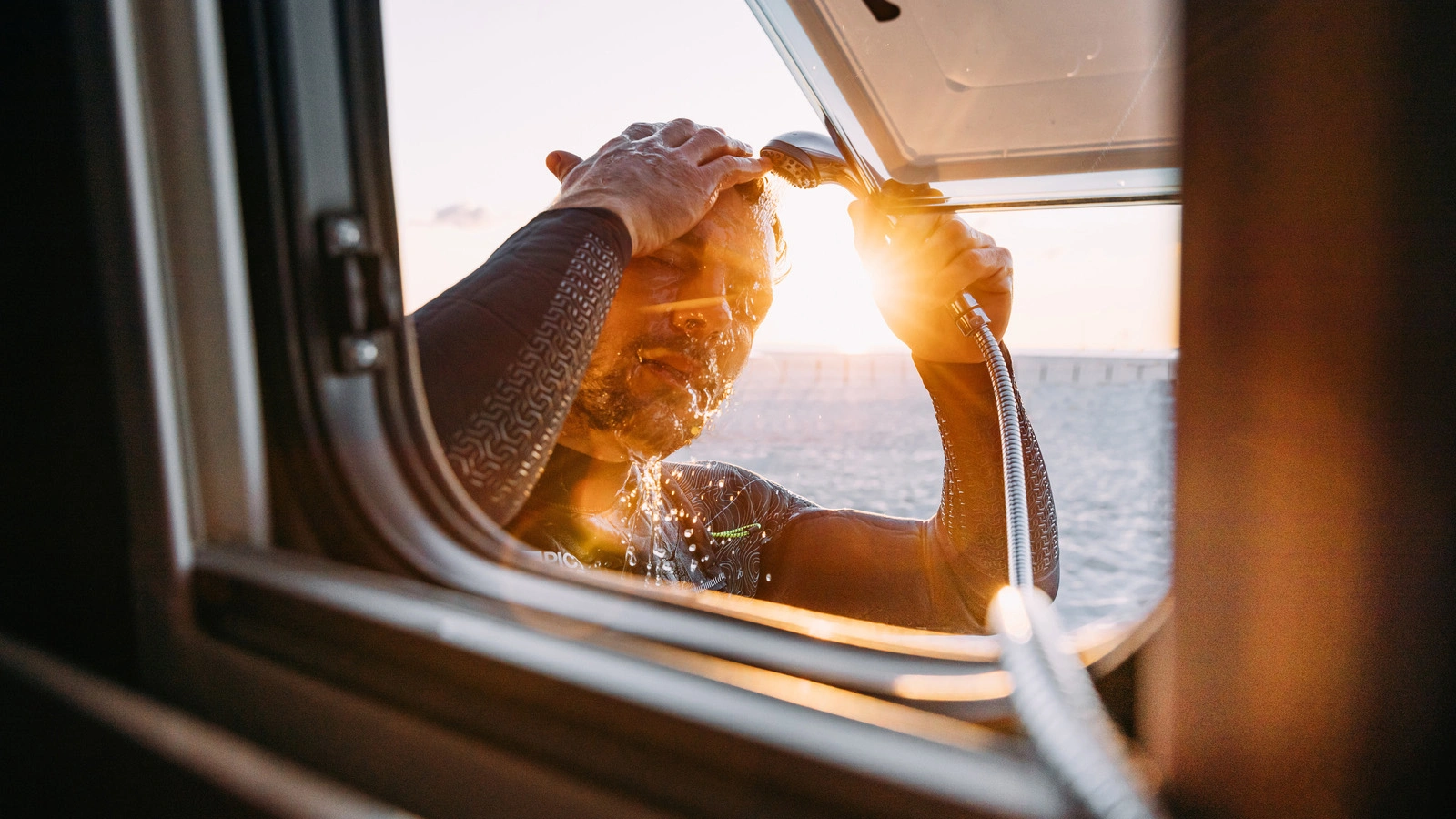 Ein Mann duscht sich im Sonnenlicht durch das Fenster eines Sunlight CLIFF 640 Campers.