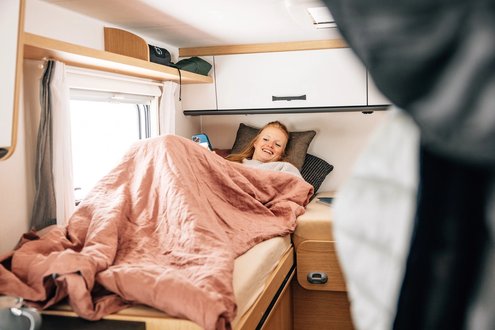 Eine Person liegt lächelnd in einem Bett im Sunlight V66 Wohnmobil.