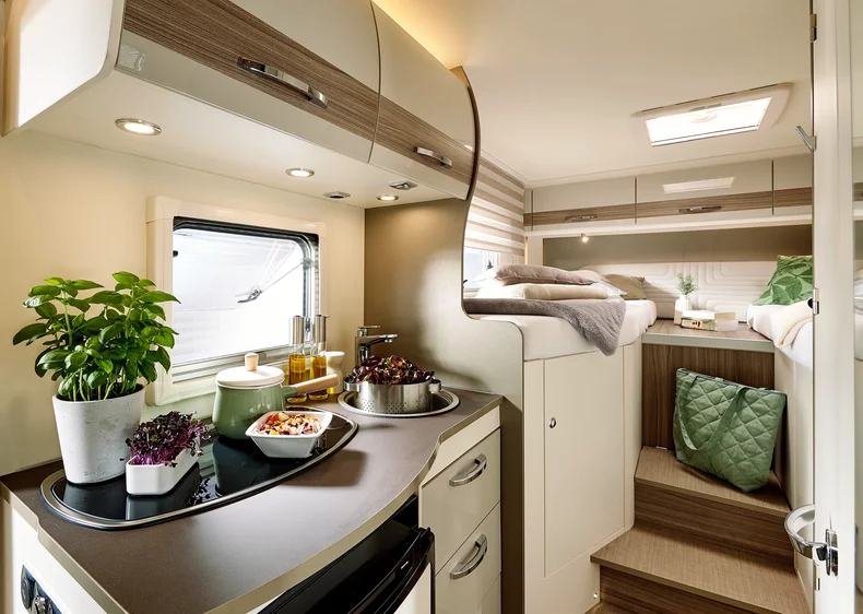 Innenansicht eines modernen Wohnmobils mit Küche und Schlafbereich.