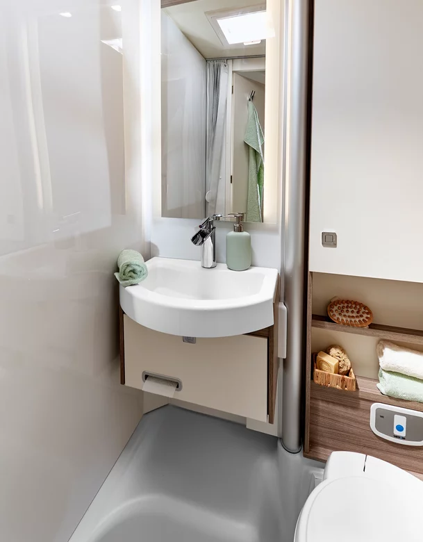 Kompaktes Badezimmer in einem Wohnmobil mit Waschbecken, Spiegel und Regalfächern.