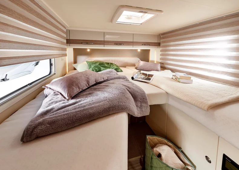 Innenraum eines Wohnmobils mit zwei Betten, Decken und Kissen.