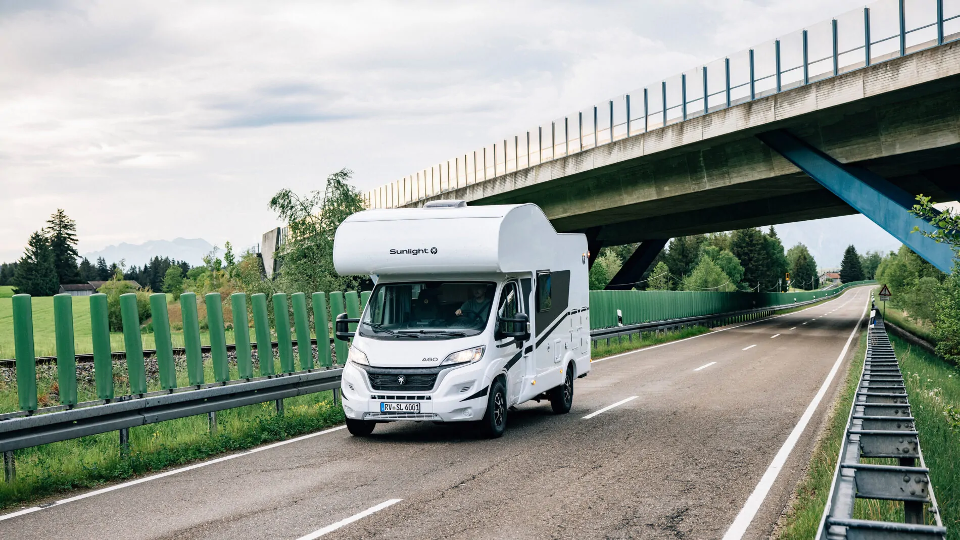 Ein weißes Sunlight A60 Wohnmobil fährt auf einer Landstraße unter einer Brücke.