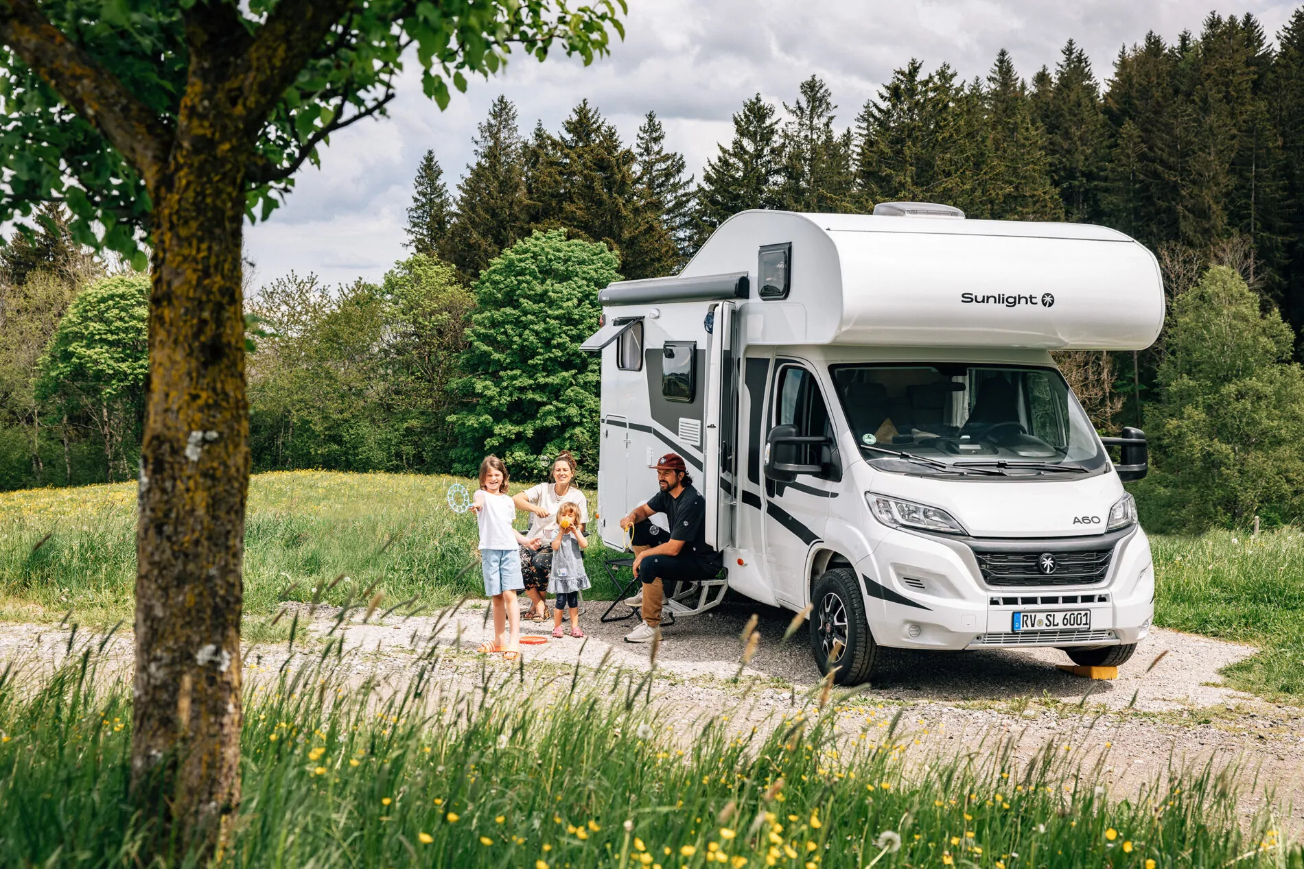 Familie steht neben einem Sunlight A60 Wohnmobil auf einem Feldweg vor einem Wald.