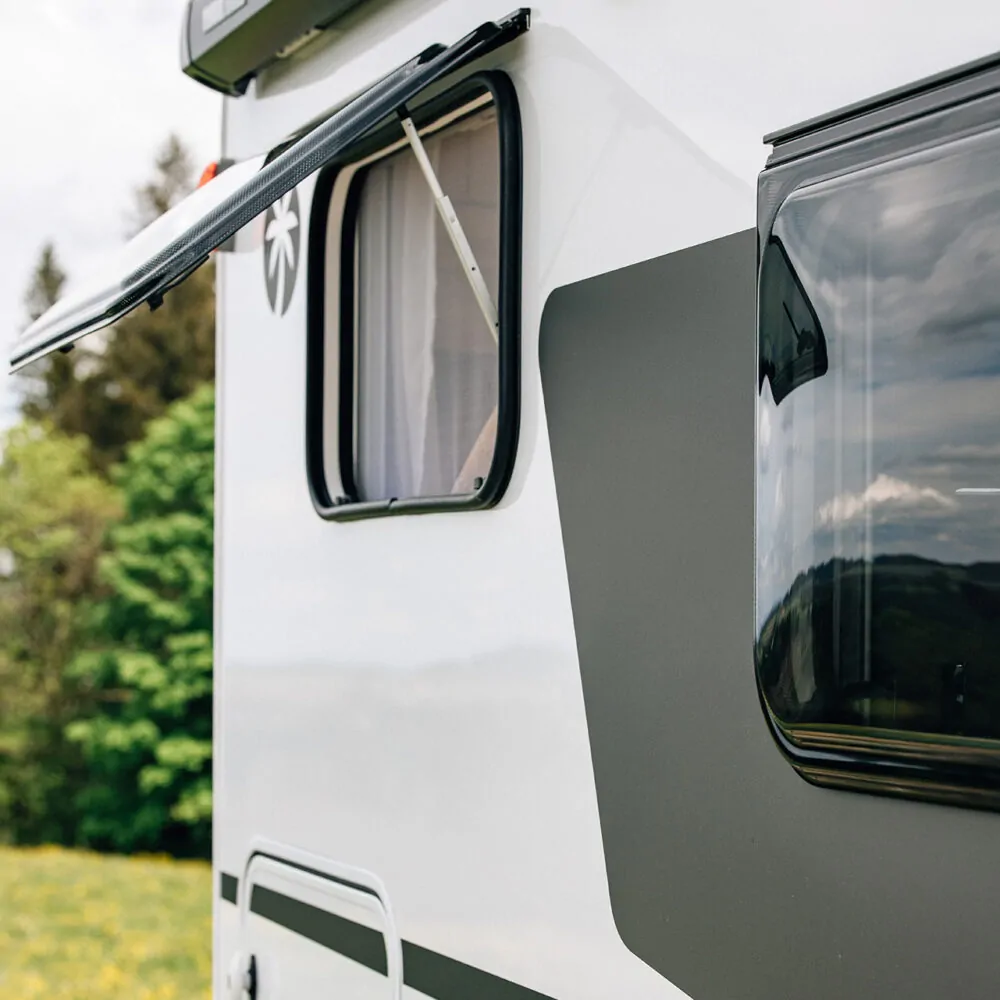 Ein Alkoven-Wohnmobil mit geöffnetem Fenster und Landschaft im Hintergrund.