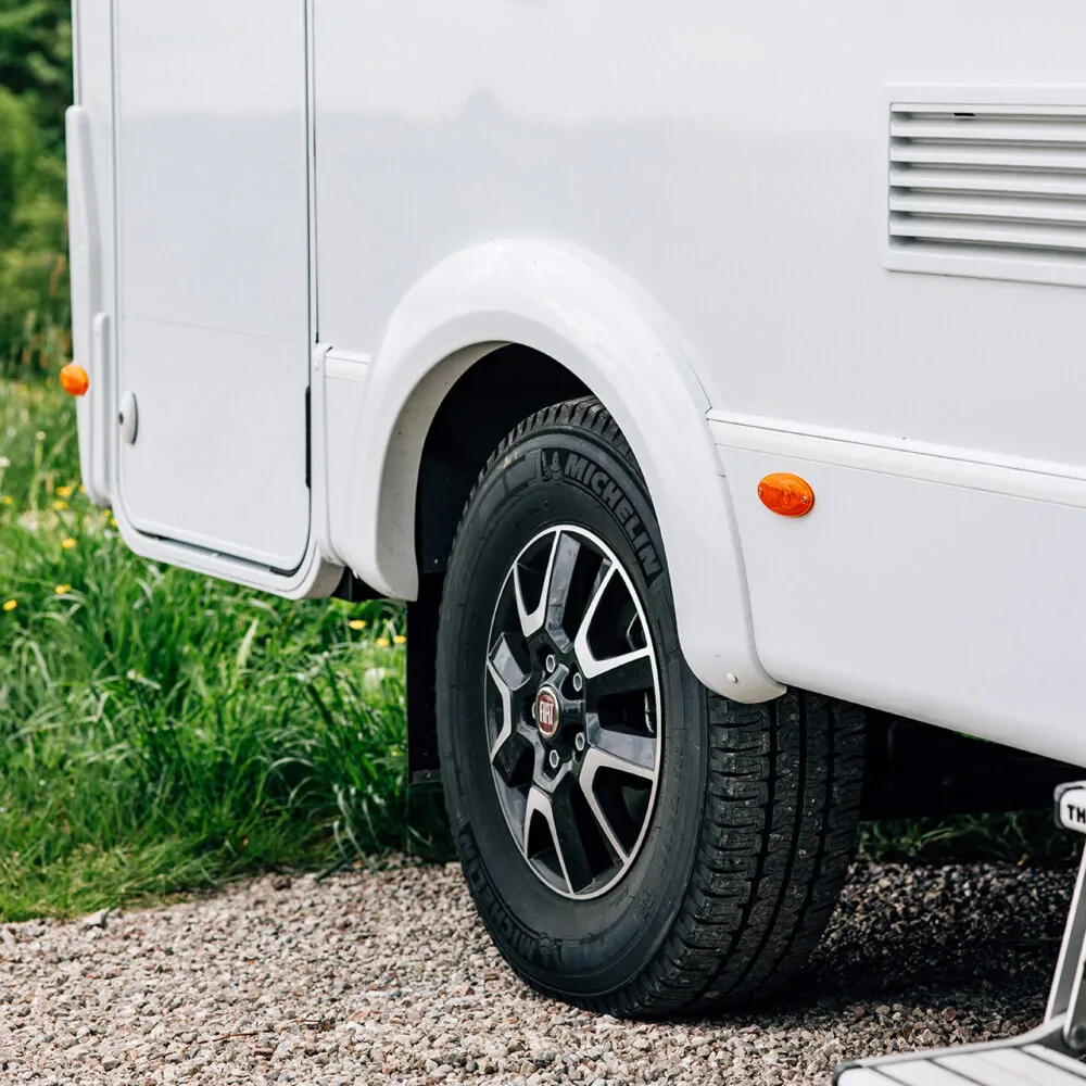 Hinterrad eines weißen Fiat-Wohnmobils auf Schotterweg.