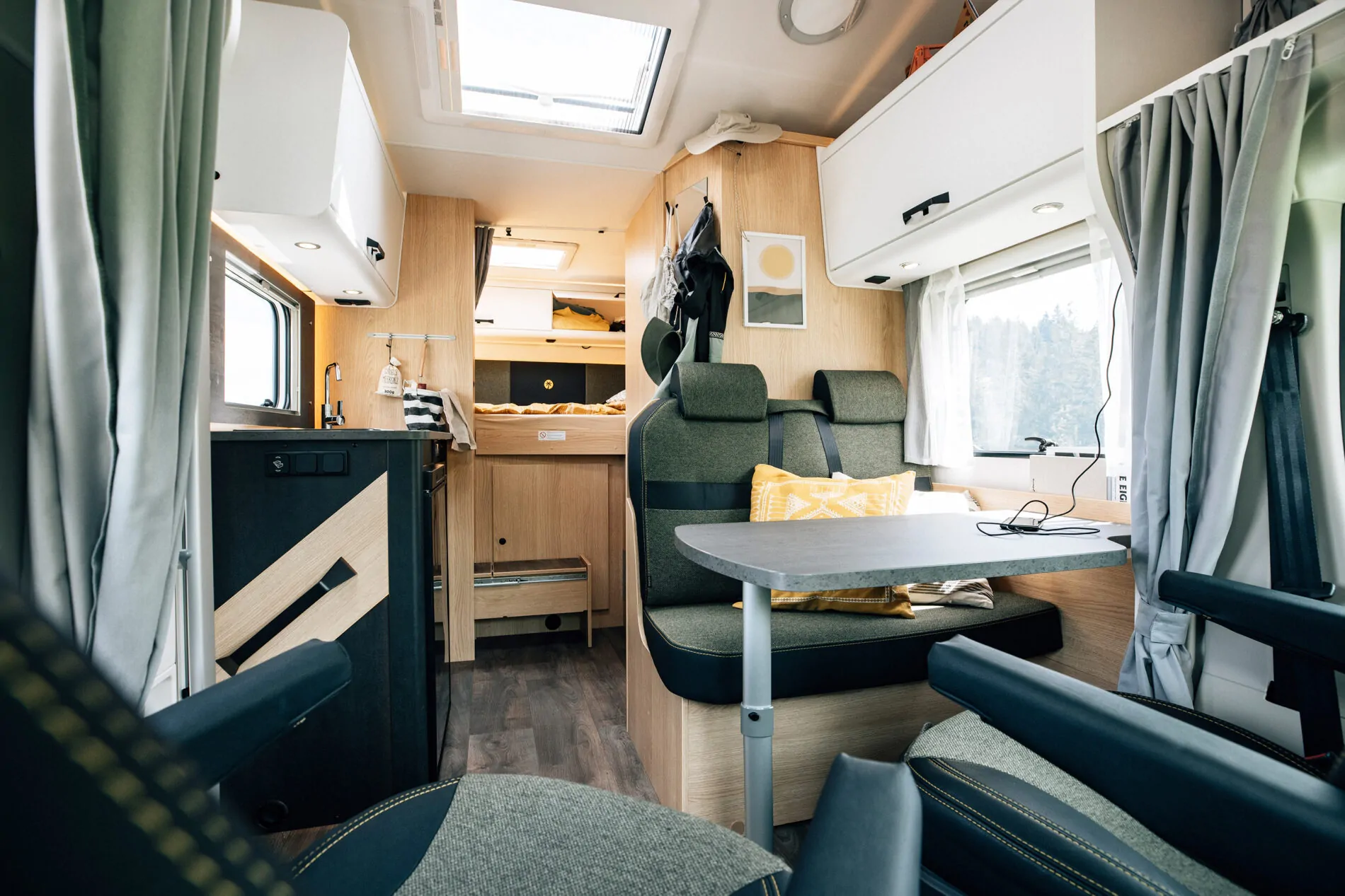 Innenraum eines Alkoven-Wohnmobils mit Sitzbereich, Tisch und Küche.