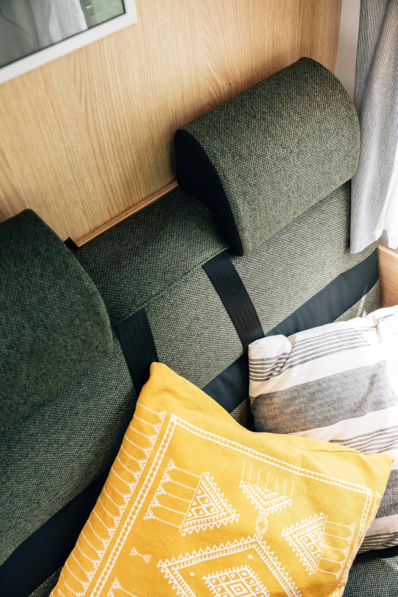 Grüne Polsterbank in einem Camper-Interieur mit gelbem und gestreiftem Kissen.