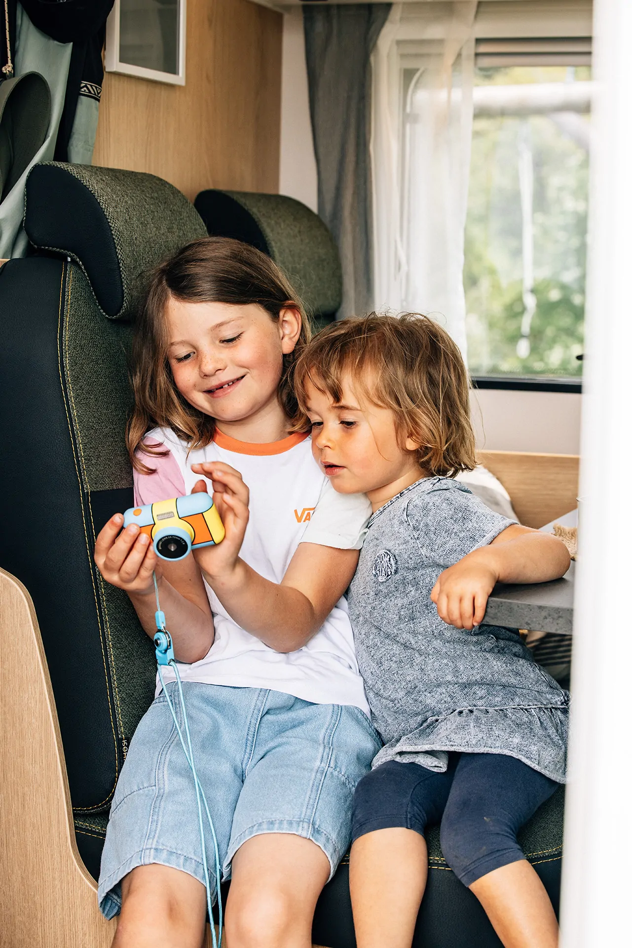 Zwei Kinder sitzen in einem Wohnmobil und schauen gemeinsam auf eine bunte Spielkamera.