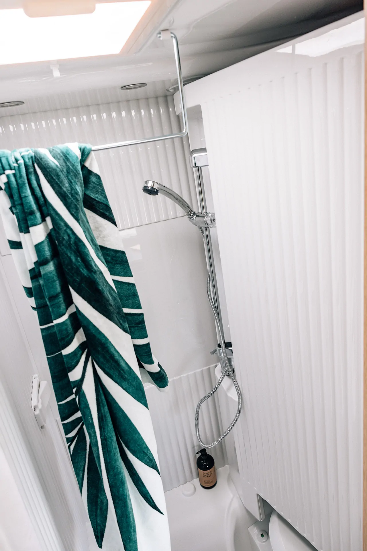 Dusche in einem Wohnmobil mit grün-weißem Handtuch und Duschkopf.
