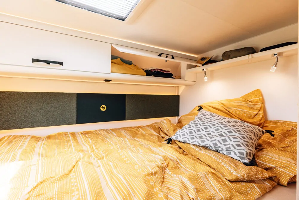 Innenraum eines Alkoven-Wohnmobils mit einem gemütlichen Bett und Regalen.