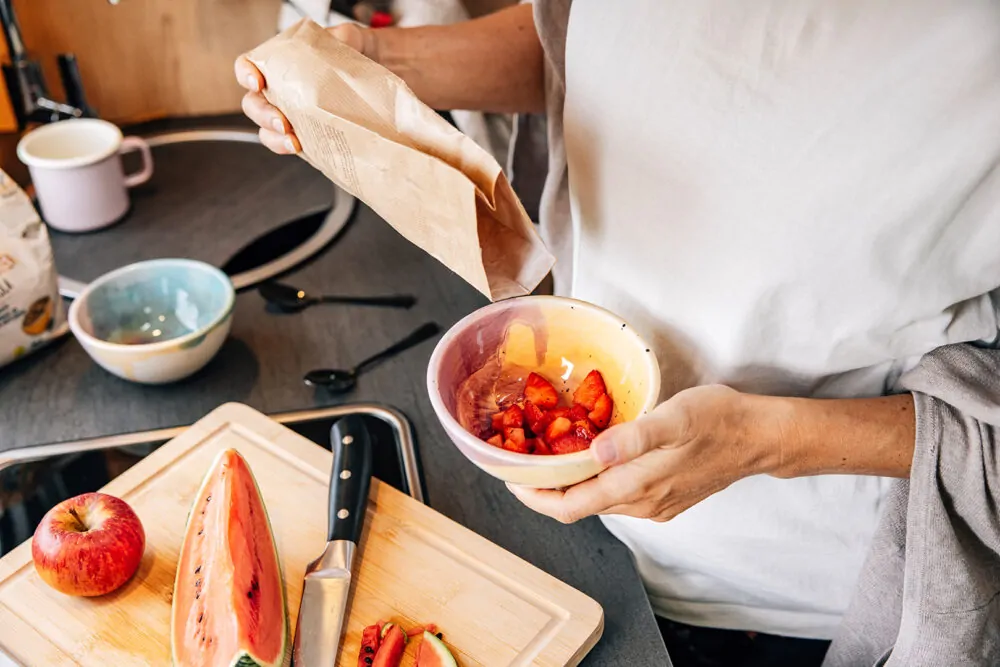 Eine Person bereitet eine Schüssel mit geschnittenen Erdbeeren in einer Küche zu.