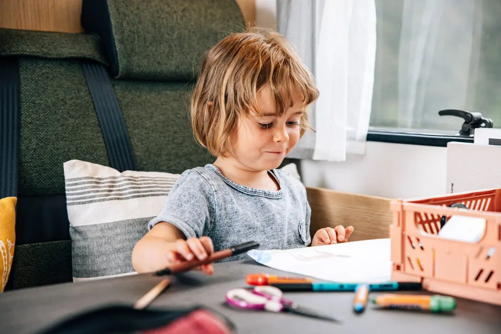 Ein Kind malt konzentriert an einem Tisch im Inneren eines Campers.