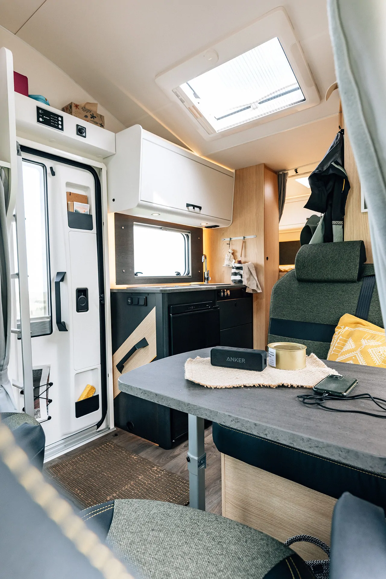 Innenansicht eines Alkoven-Campers mit Tisch, Sitzgelegenheiten und Küchenzeile.
