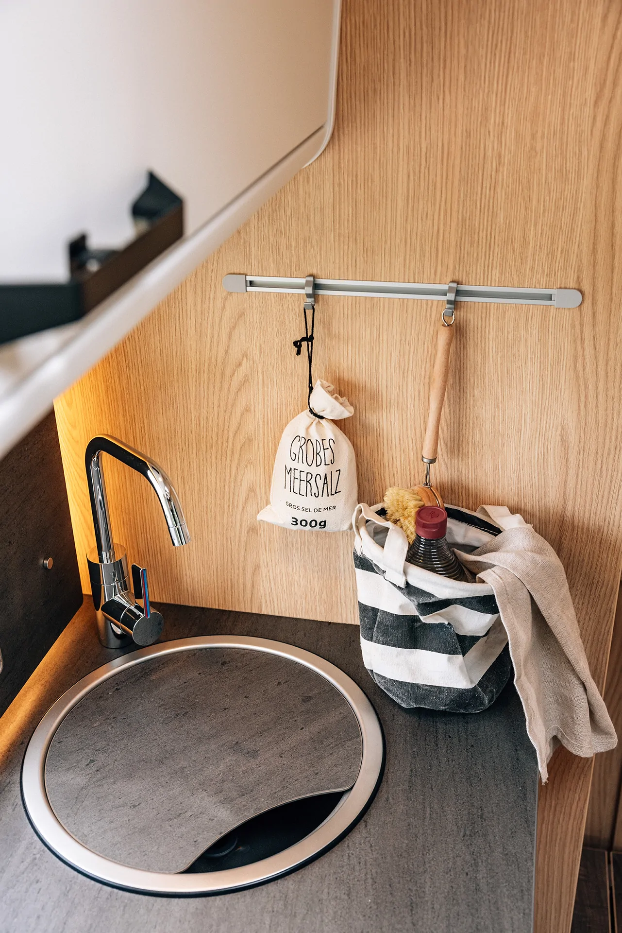 Küchenbereich mit rundem Spülbecken, Wasserhahn, Meersalzbeutel und gestreifter Tasche.