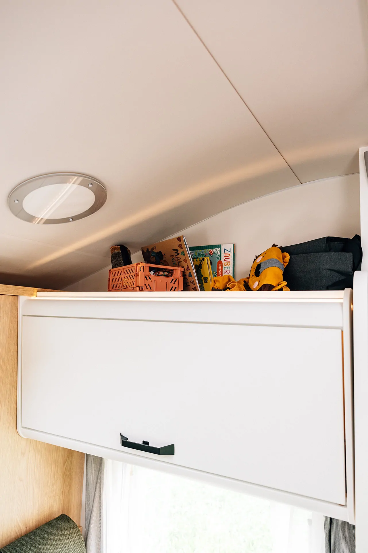 Oberes Fach eines Wohnmobils mit Büchern, Spielzeug und Aufbewahrungsboxen.