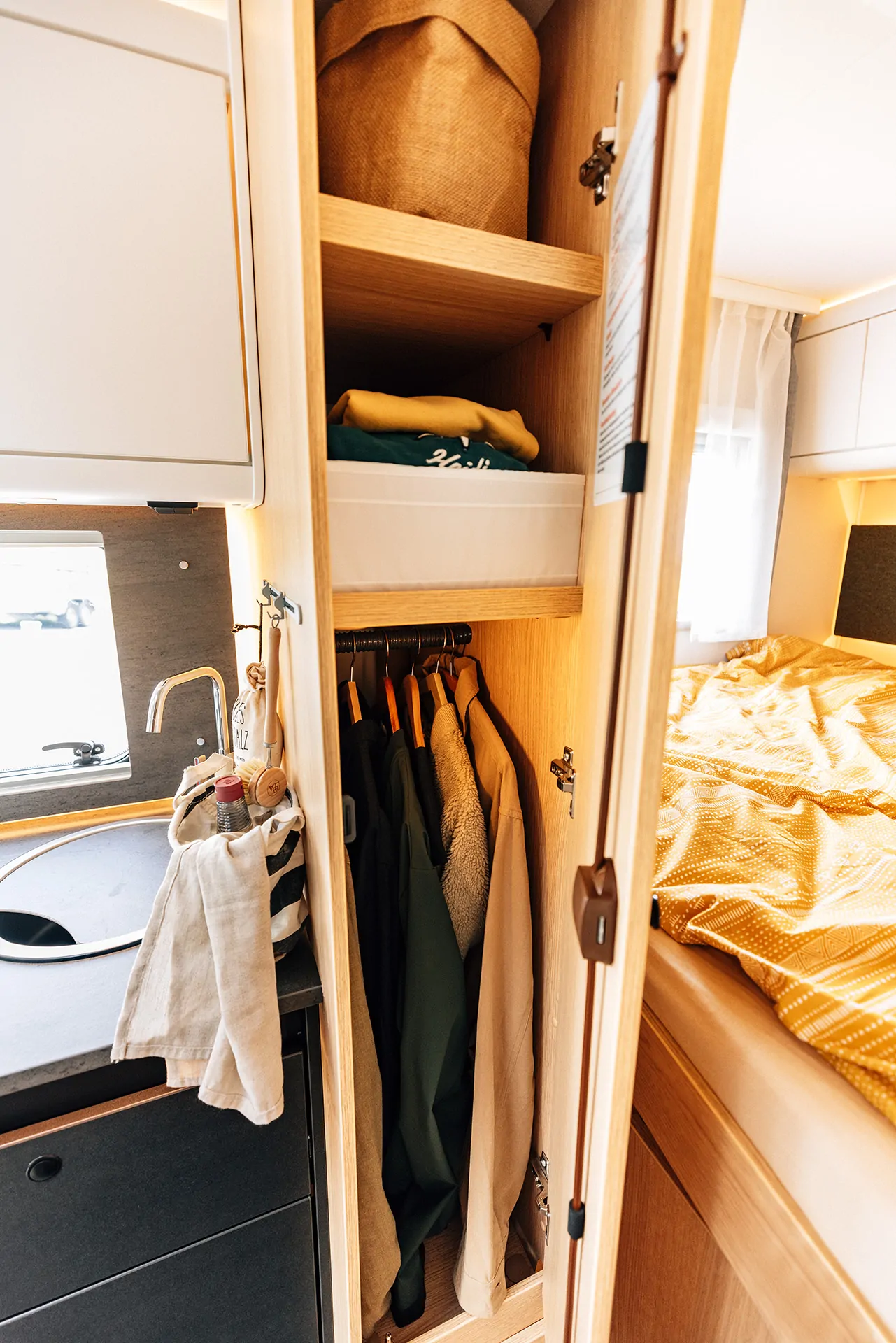 Innenraum eines Campers mit Kleiderschrank, Küchenzeile und Bett.