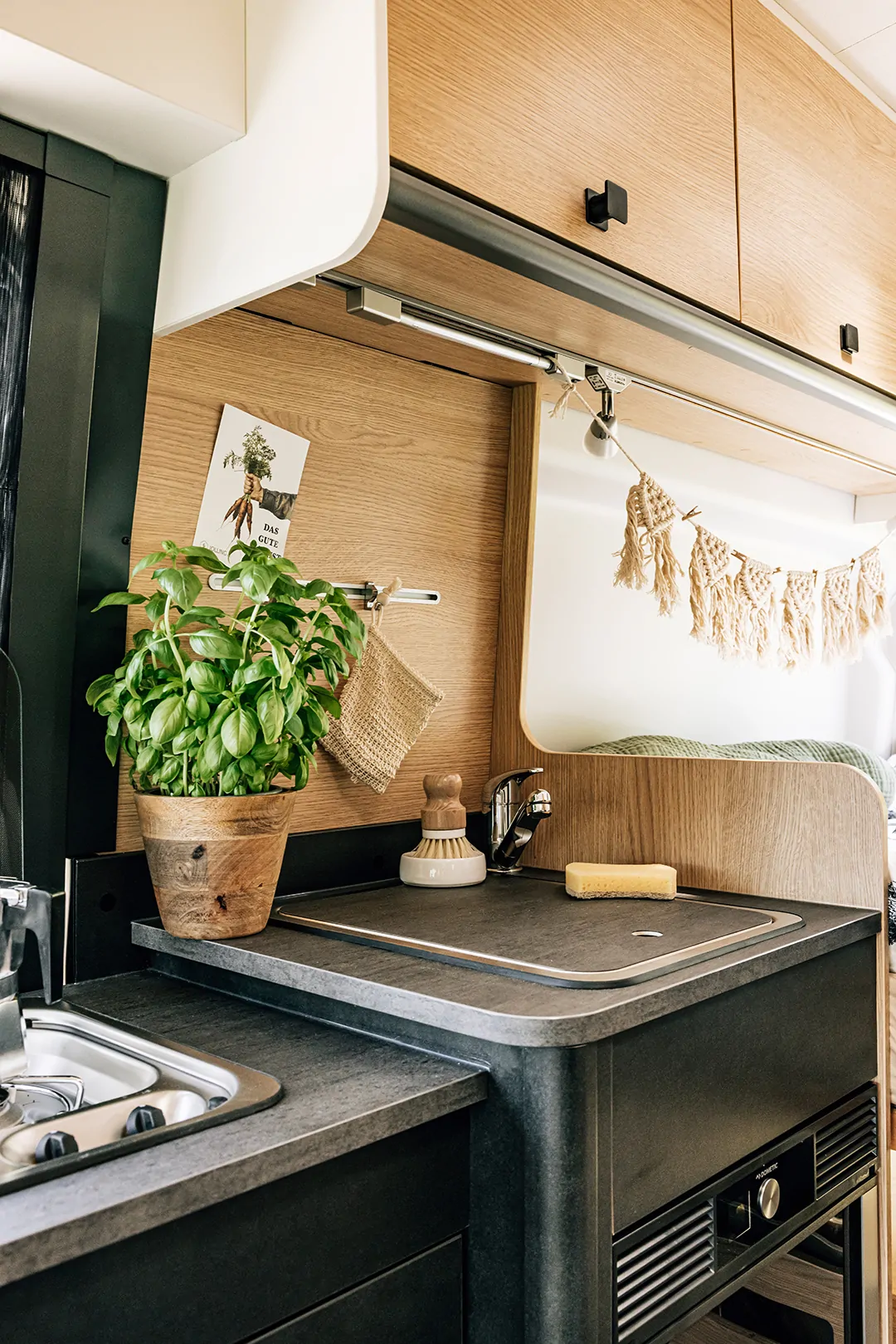 Innenraum einer Wohnmobilküche mit Spüle, Basilikumtopf und Dekoration.