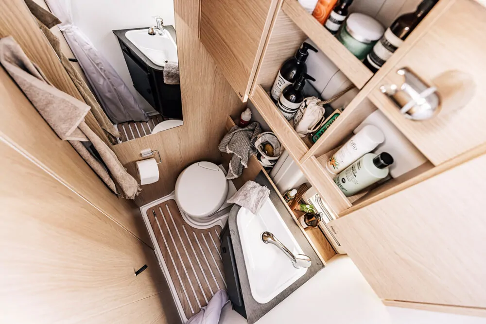 Kompaktes Badezimmer in einem Camper mit Waschbecken, Toilette und Regalen.