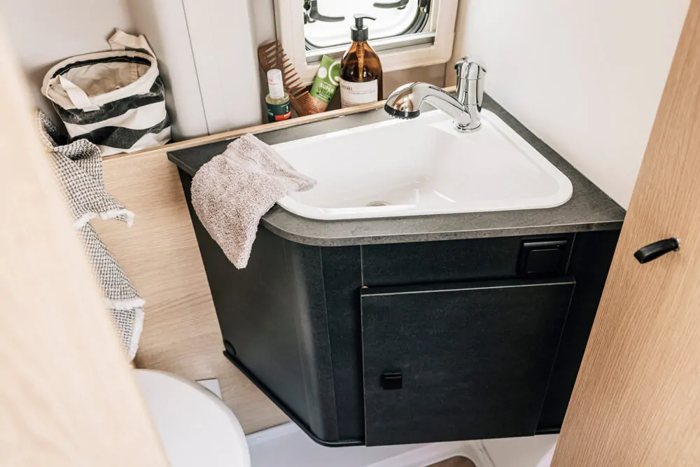 Waschbecken in einem kompakten Badezimmer eines Campers mit Pflegeprodukten auf der Ablage.