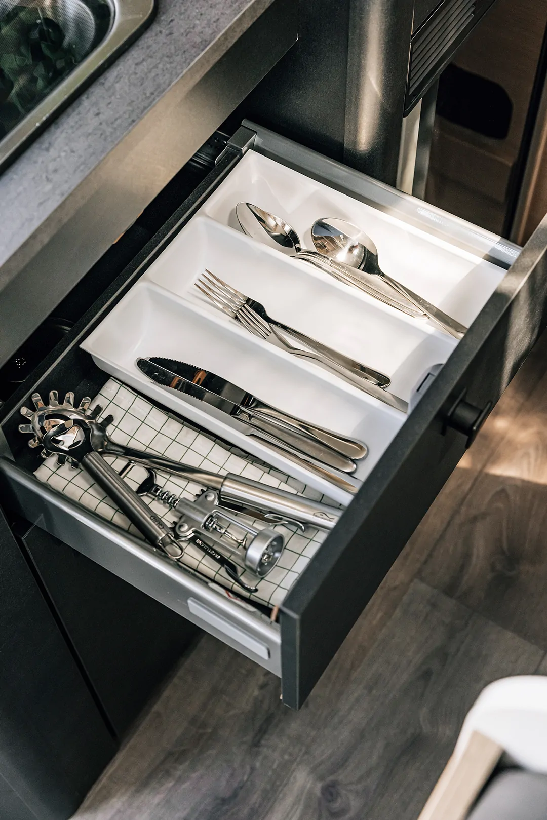 Offene Besteckschublade mit Löffeln, Gabeln, Messern und Küchenwerkzeugen.