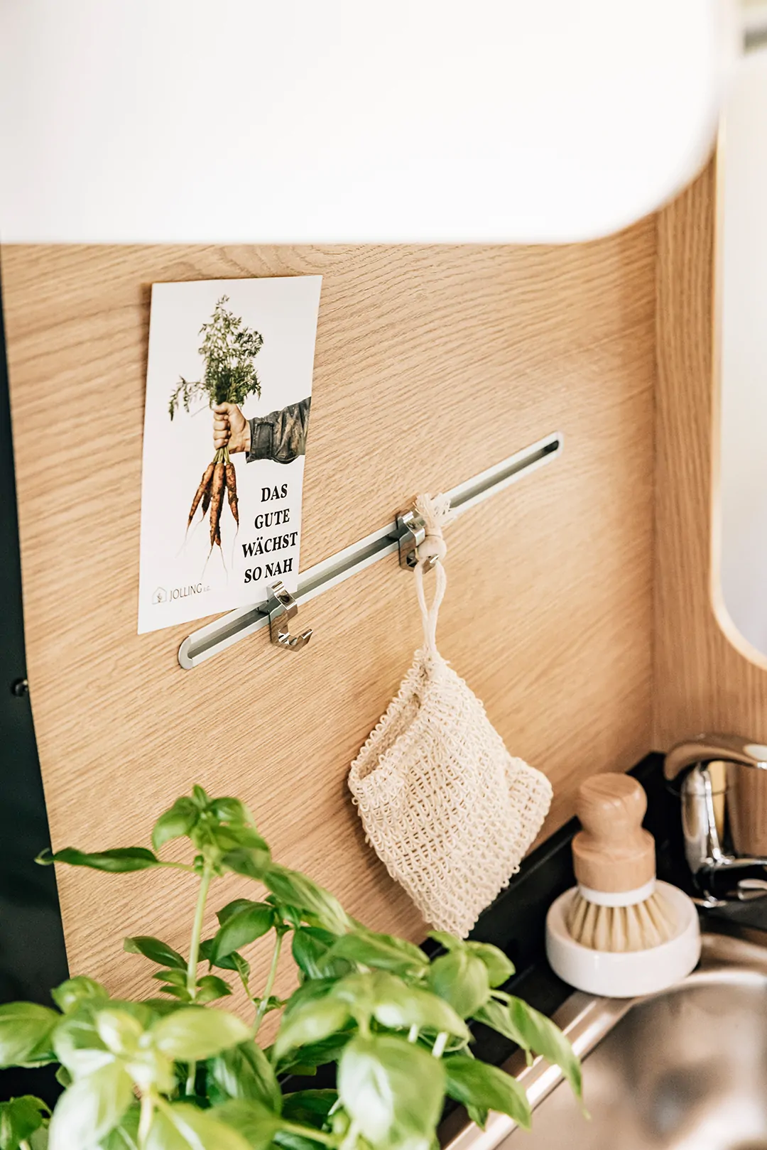 Eine Küche mit einem Holzbrett, an dem ein Poster mit Karottenmotiv hängt, und Basilikum im Vordergrund.