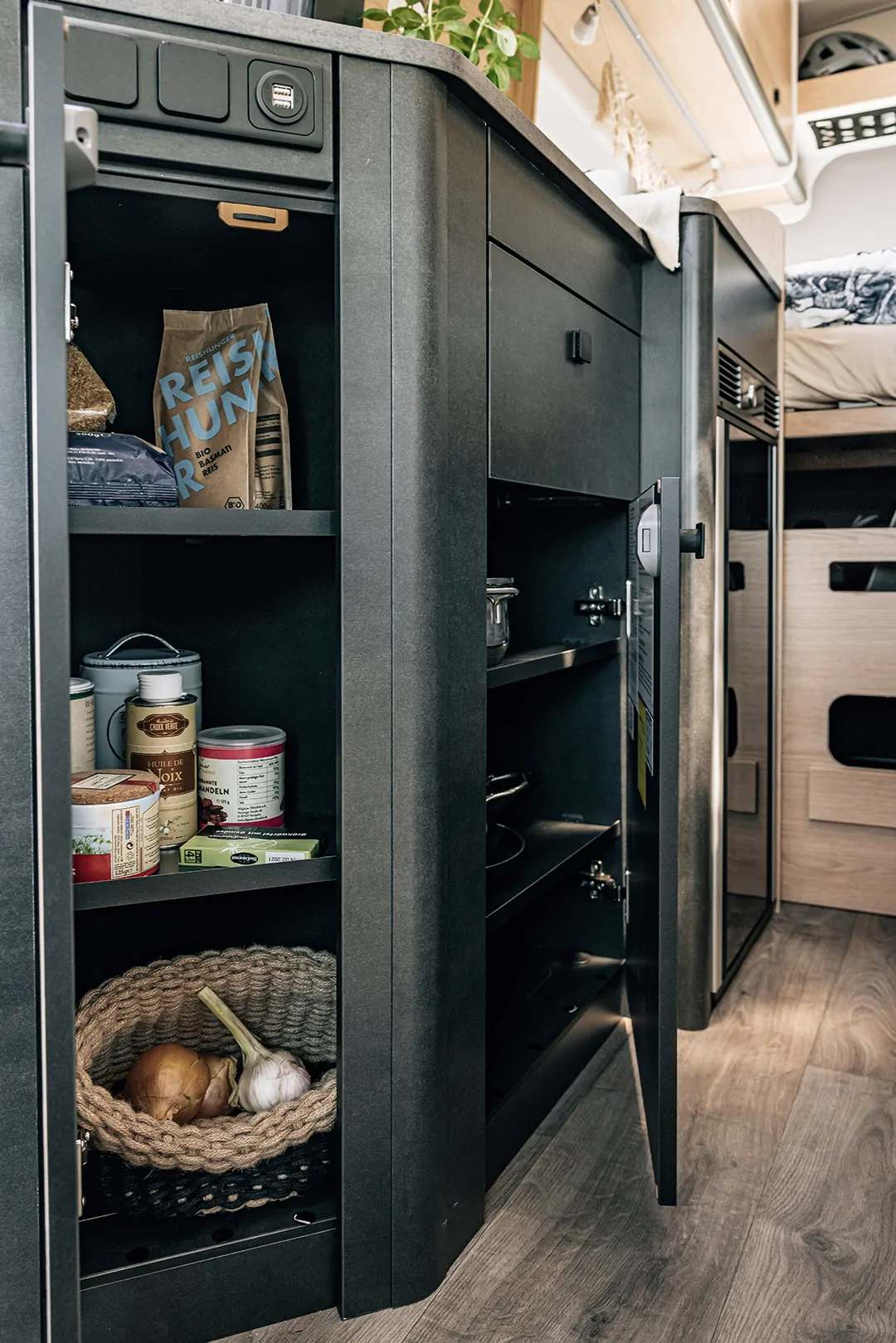 Offener Küchenschrank in einem Camper mit Lebensmitteln und Küchenutensilien.