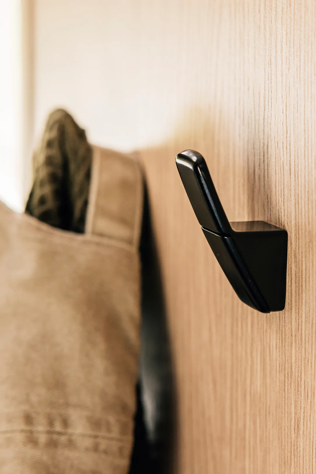 Schwarzer Kleiderhaken an einer Holzwand mit aufgehängtem Kleidungsstück.