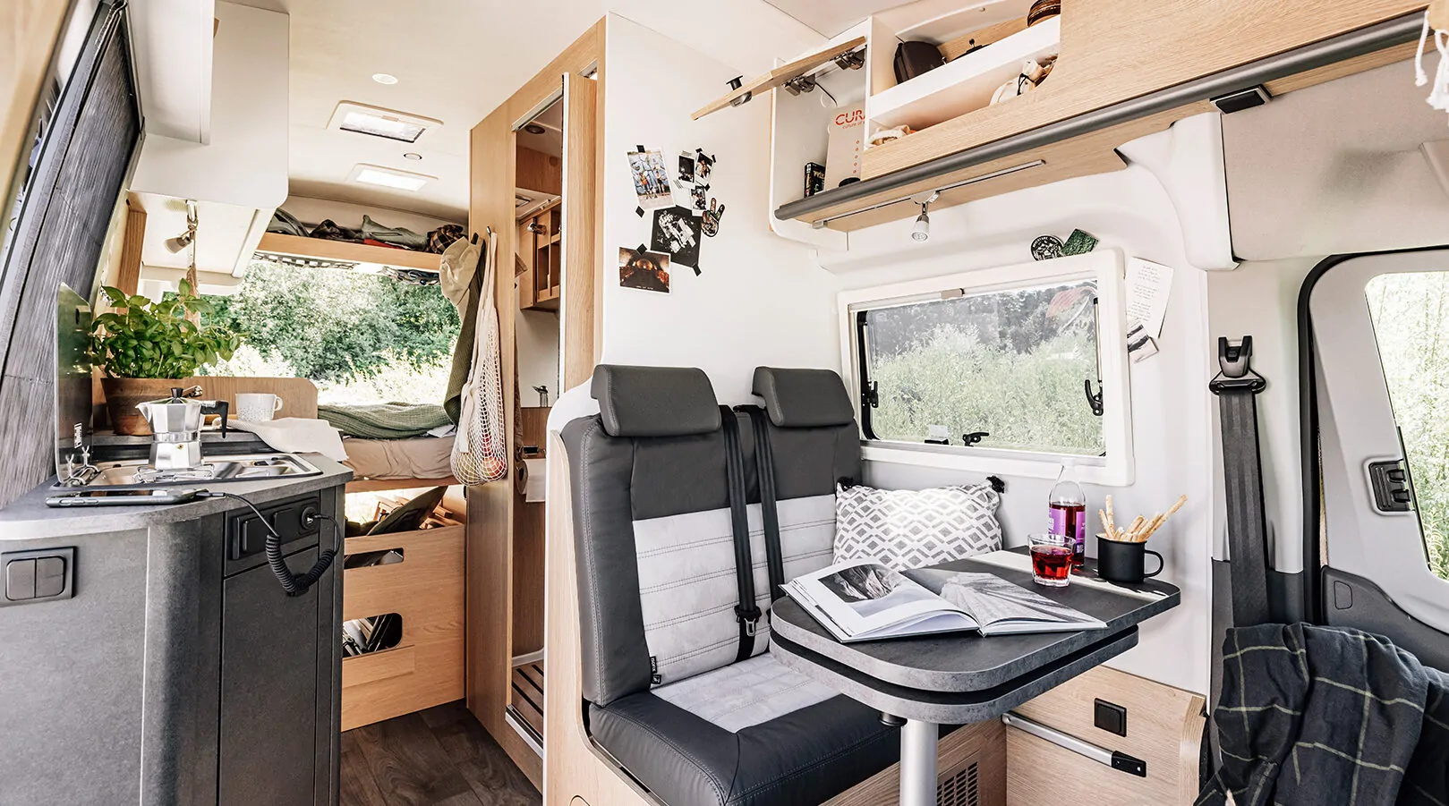 Innenraum eines Wohnmobils mit Küche, Sitzbereich und Bett im Hintergrund.