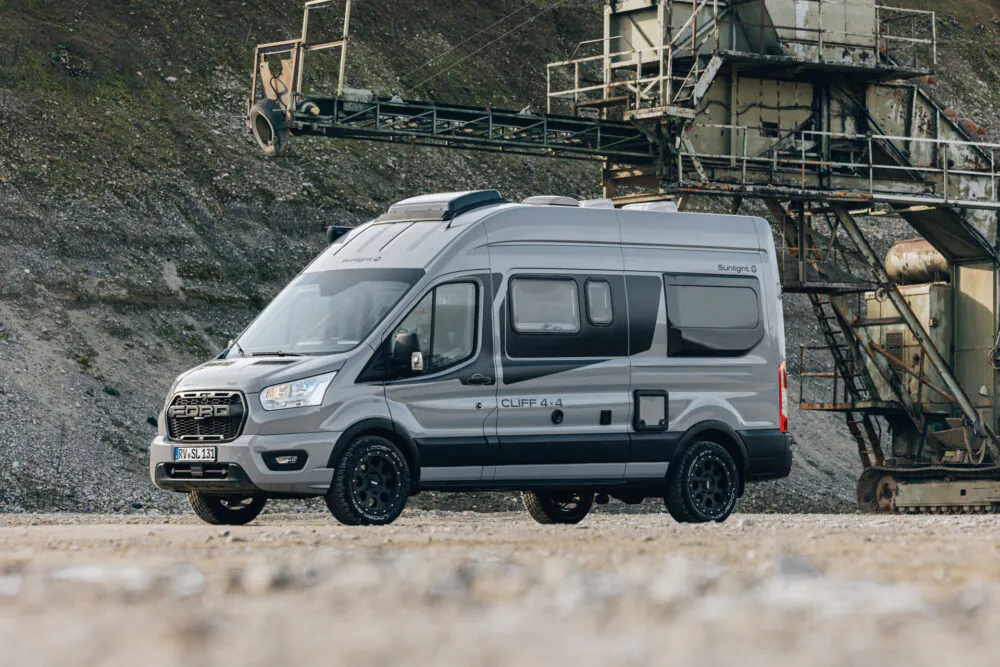 Ein grauer Sunlight Cliff 4x4 Camper steht vor einer industriellen Anlage.