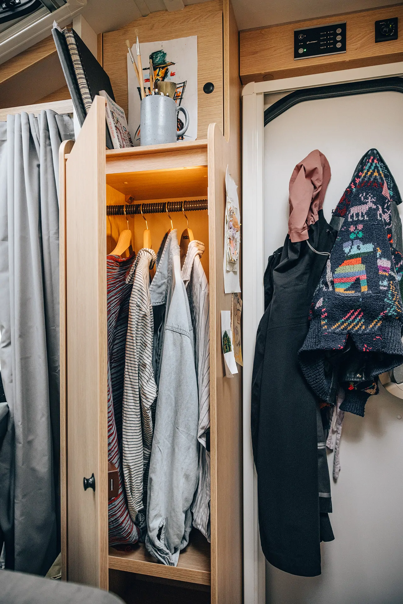 Ein Kleiderschrank in einem Wohnmobil mit hängender Kleidung und Jacken an der Tür.