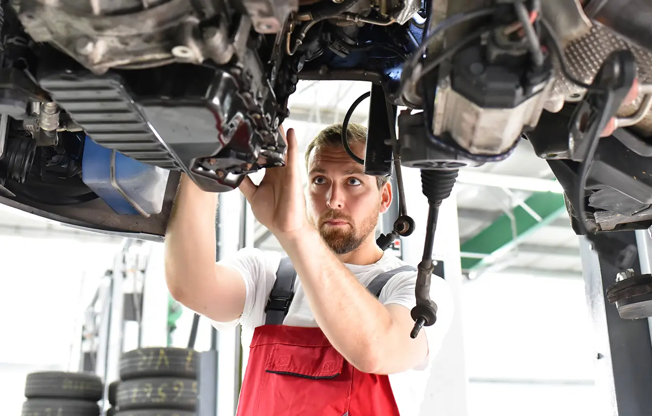 Ein Mechaniker in roter Latzhose arbeitet unter einem Fahrzeug.
