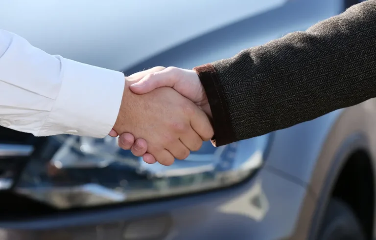 Zwei Personen schütteln sich vor einem Auto die Hände.