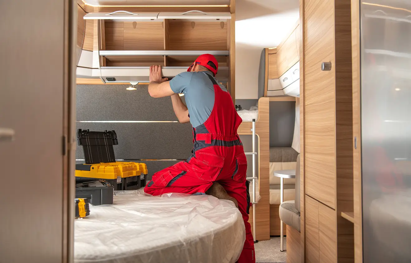 Ein Handwerker in roter Arbeitskleidung arbeitet an einem Schrank in einem Camper.