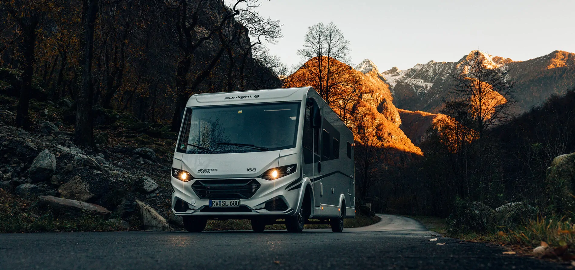 Ein Sunlight Adventure Edition Wohnmobil fährt auf einer Straße durch eine herbstliche Berglandschaft.